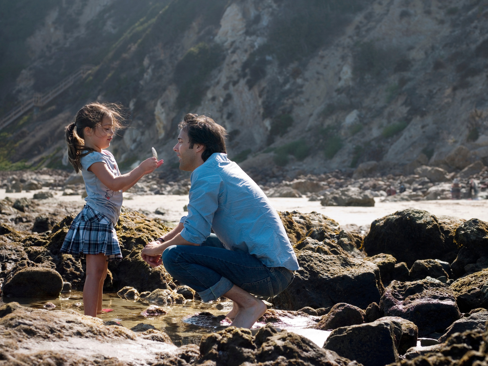 A young child shows their parent a seashell on the beach.