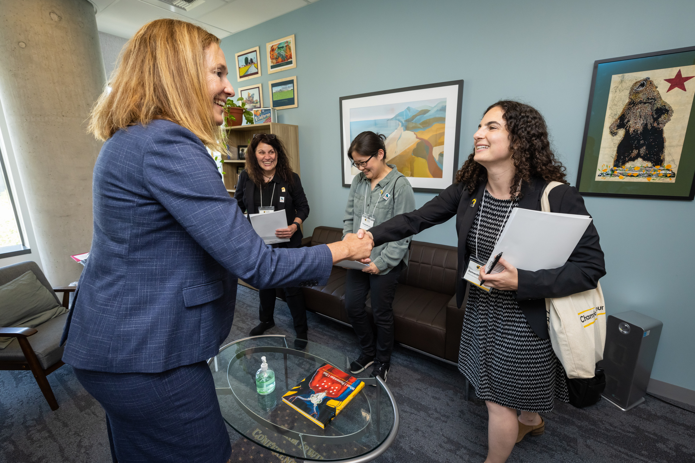 Assemblymember Jacqui Irwin shakes hands with California State Parks Foundation staff member Samantha Joseph in a meeting in her office at Park Advocacy Day. Two other people stand in the background of the meeting laughing.
